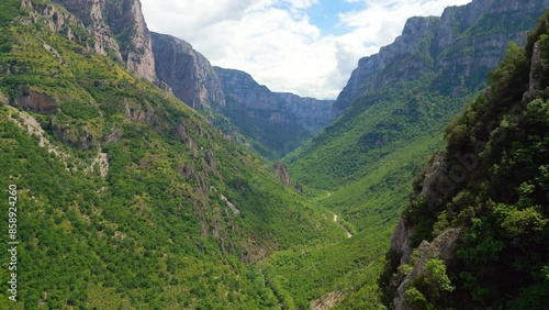 A breathtaking aerial view of the Vikos Gorge in Greece, showcasing the dramatic cliffs and the winding Voidomatis river snaking through the lush green valley.