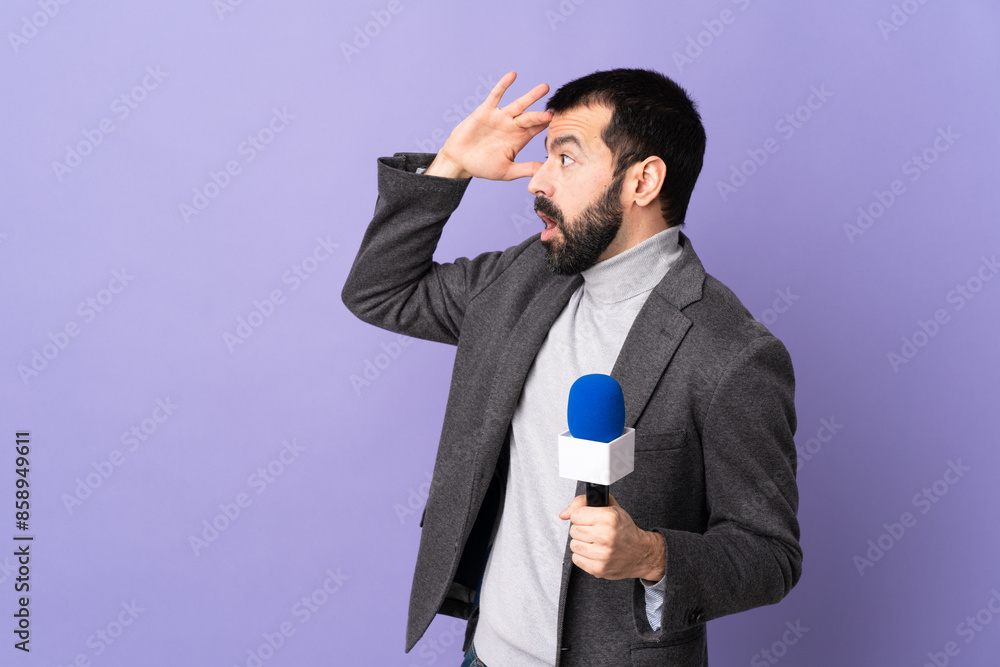 Adult reporter man with beard holding a microphone over isolated purple background with surprise expression while looking side Adult reporter man with beard holding a microphone over isolated purple background with surprise expression while looking side