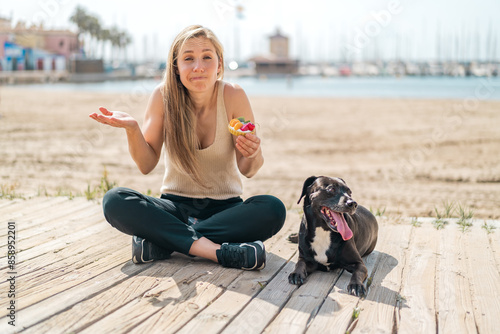 Young blonde woman with her dog holding a tartlet at outdoors making doubts gesture while lifting the shoulders © luismolinero