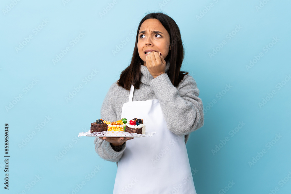 Pastry chef holding a big cake over isolated blue background is a little bit nervous. Pastry chef holding a big cake over isolated blue background is a little bit nervous.