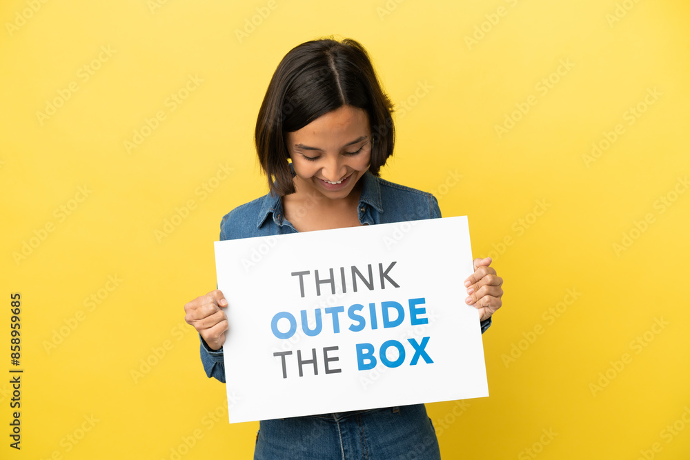 Young mixed race woman isolated on yellow background holding a placard with text Think Outside The Box Young mixed race woman isolated on yellow background holding a placard with text Think Outside The Box