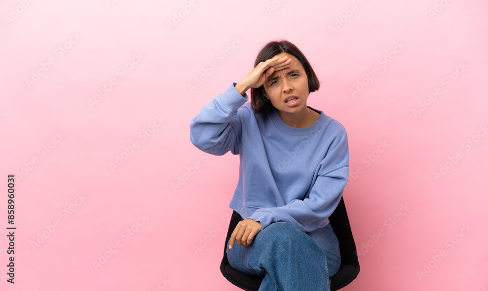 Young mixed race woman sitting on a chair isolated on pink background looking far away with hand to look something
