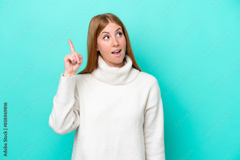 Young redhead woman isolated on blue background intending to realizes the solution while lifting a finger up Young redhead woman isolated on blue background intending to realizes the solution while lifting a finger up