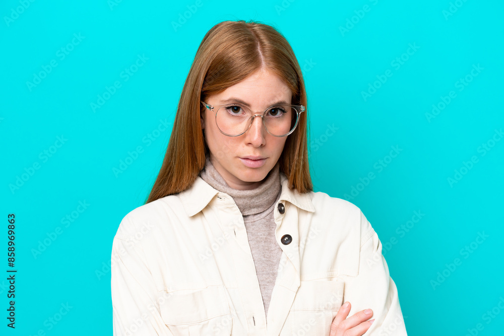 Young redhead woman isolated on blue background With glasses and arms crossed Young redhead woman isolated on blue background With glasses and arms crossed