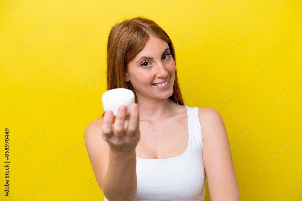 Young redhead woman isolated on yellow background with moisturizer and offering it Young redhead woman isolated on yellow background with moisturizer and offering it