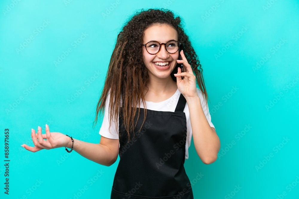 Restaurant waiter Arab woman isolated on blue background keeping a conversation with the mobile phone with someone Restaurant waiter Arab woman isolated on blue background keeping a conversation with the mobile phone with someone