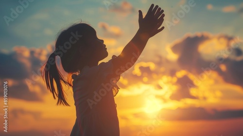 Silhouette of kid child girl raised hands worship pray. Kid girl praying in the sunset sky for a new day freedom