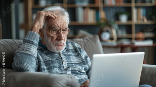 thoughtful upset elderly caucasian man 70 years old holding his head and looking at laptop screen while at home, concept of pensioners being deceived by cyber fraudsters