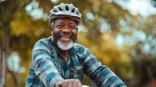 The stylish senior African American cycled around the park, wearing a helmet and dressed casually. A smiling mature black male rides a bicycle enjoying the outdoors on a sunny day