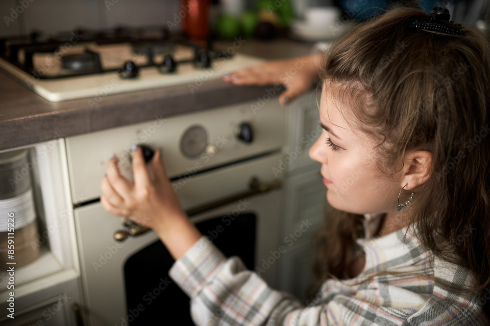 Rare view closeup indoor portrait of young female in kitchen, switching stove on by turning knob and adjusting right temperature, going to cook pie or pudding for dinner or breakfast Rare view closeup indoor portrait of young female in kitchen, switching stove on by turning knob and adjusting right temperature, going to cook pie or pudding for dinner or breakfast