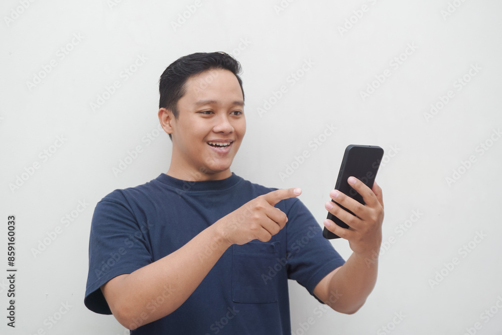 Young Asian man smiling and pointing to smartphone isolated on white background. lifestyle and advertising concept. Men using blue shirt holding phone Young Asian man smiling and pointing to smartphone isolated on white background. lifestyle and advertising concept. Men using blue shirt holding phone