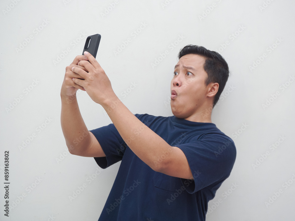Young Asian man looking smartphone with shocked and surprised expression. Male with blue t-shirt showing excited expression isolated on white background Young Asian man looking smartphone with shocked and surprised expression. Male with blue t-shirt showing excited expression isolated on white background