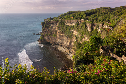 View from the high cliffs of Uluwatu in Bali Island in Indonesia. Endless ocean around, the abyss and surf is below, the stee rocky cliffs are covered with tropical greenery. photo