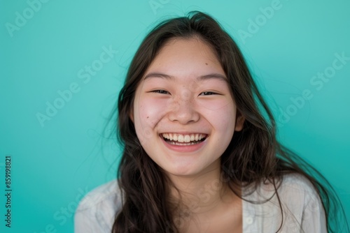 Joyful Laughter: Portrait of a Happy Young Asian Woman with Long Hair and Blue Background