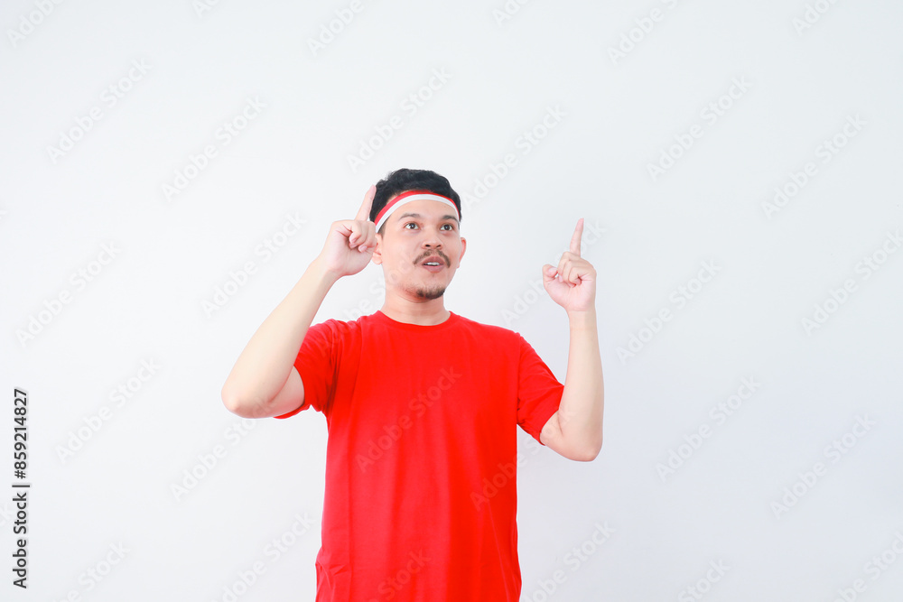 Smiling young Asian man in casual t-shirt pointing finger aside at copy space. indonesian independence day celebration concept Smiling young Asian man in casual t-shirt pointing finger aside at copy space. indonesian independence day celebration concept