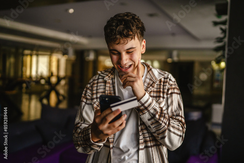 Young boy stand and buy online on mobile phone with credit card