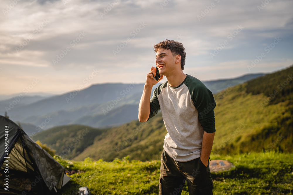 Young boy stand in front tent and talk on mobile phone on the mountain