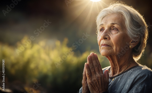 old wise woman with praying hands and with rays of light like Christian Catholic belief concept 