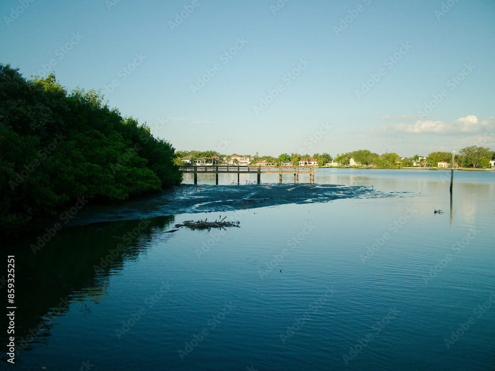Wide view of Coffee Pot Park bayou in St. Petersburg, Florida with blue water and sky. Wood dock on the left side on a sunny day. Near sunset with reflections. Looking south on a calm day in St. Pete Wide view of Coffee Pot Park bayou in St. Petersburg, Florida with blue water and sky. Wood dock on the left side on a sunny day. Near sunset with reflections. Looking south on a calm day in St. Pete