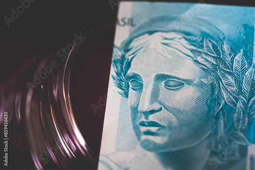 Uma nota de 100 reais em fotografia macro sobre um cofrinho de vidro em fundo escuro ou sombrio. Crise financeira, falta de crédito.