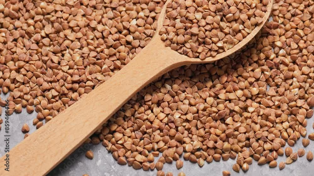 Dry Buckwheat in Wooden Spoon and Scattered Buckwheat Grains on Gray Background, Handheld Shot Dry Buckwheat in Wooden Spoon and Scattered Buckwheat Grains on Gray Background, Handheld Shot