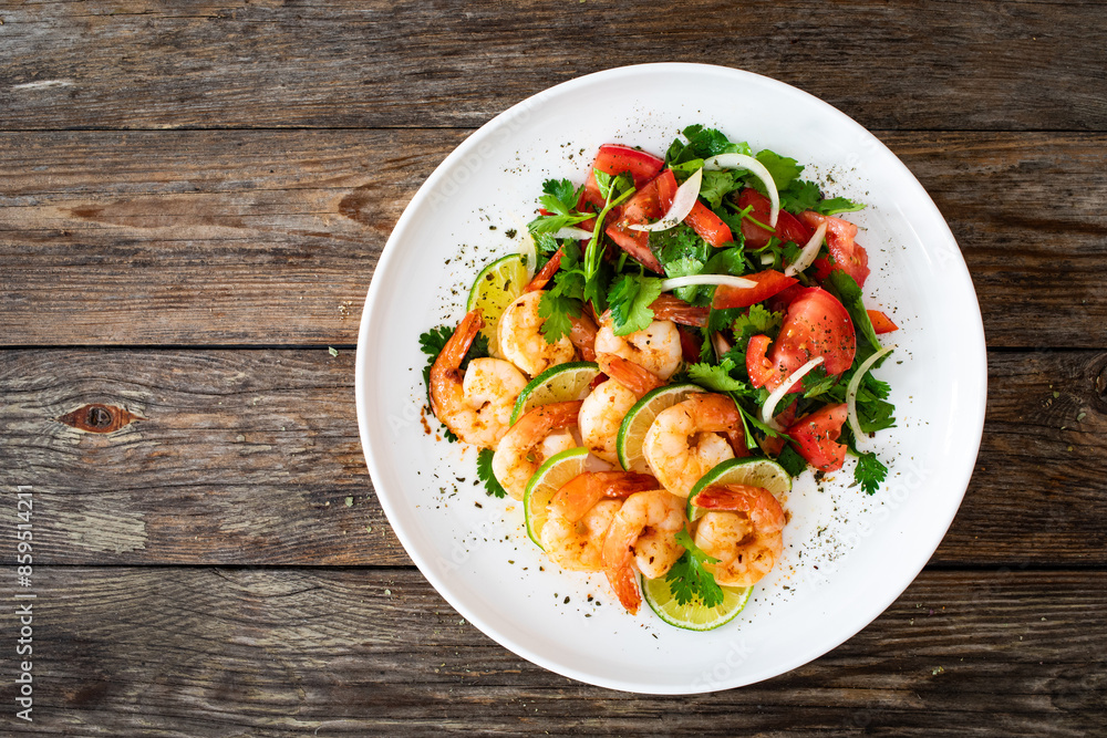 Fried shrimps with garlic, lime and fresh vegetables served on white plate on wooden table
Fried shrimps with garlic, lime and fresh vegetables served on white plate on wooden table