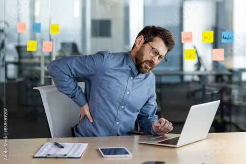 Cuadro en lienzo Suffering from overtired young man in the office at the table, sitting holding h