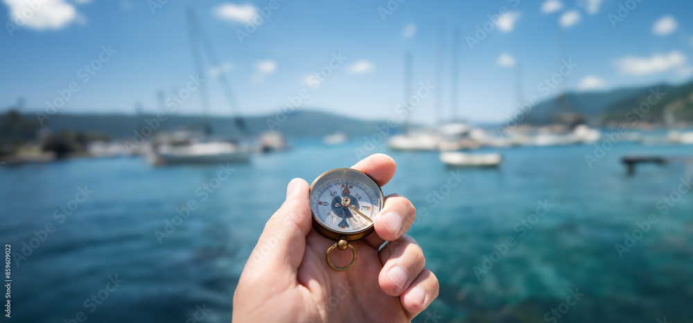 Compass in hand on the background of yachts and the sea. Background on the theme of travel, navigation, voyage, hike, etc. Shallow depth of field, sharpness on the compass. Compass in hand on the background of yachts and the sea. Background on the theme of travel, navigation, voyage, hike, etc. Shallow depth of field, sharpness on the compass.