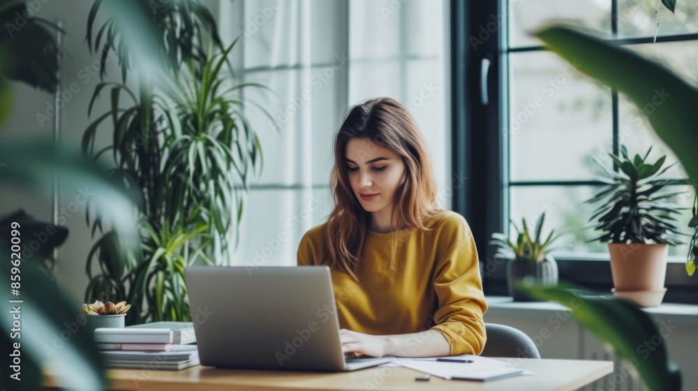 A young woman is seated at a modern desk, using a sleek laptop A young woman is seated at a modern desk, using a sleek laptop