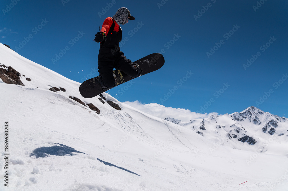 A woman snowboarder makes a ski jump against the backdrop of high snow-capped mountains A woman snowboarder makes a ski jump against the backdrop of high snow-capped mountains