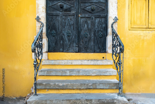 Fototapeta Naklejka Na Ścianę i Meble -  Yellow color building wall and black entrance door, stairs and railing, old house entrance