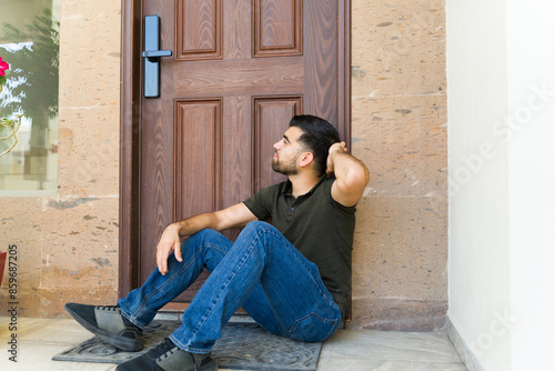 Young man locked out of his house and sitting and waiting next to his door for someone else to open