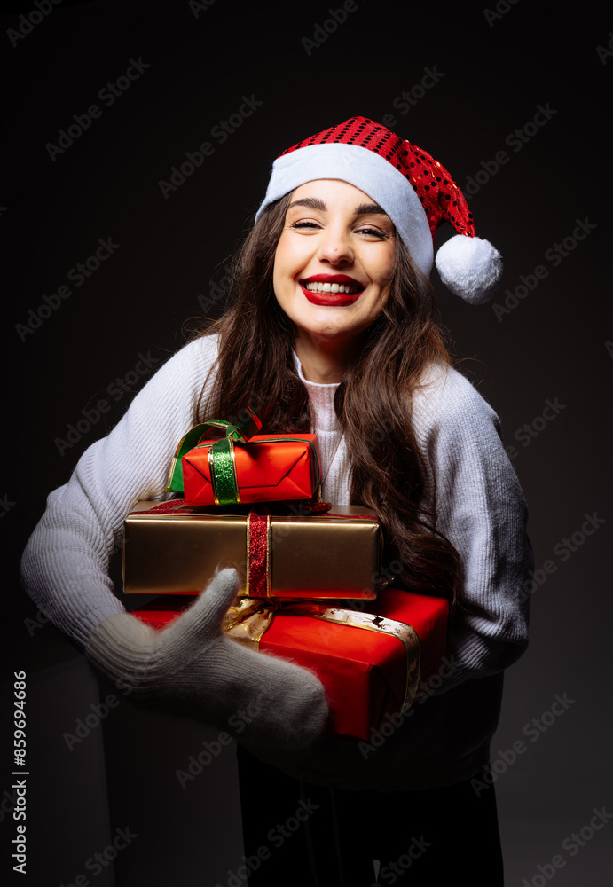 Woman in Santa Hat Holding Christmas Gifts. A woman wearing a Santa hat smiles while holding a stack of wrapped Christmas gifts. Woman in Santa Hat Holding Christmas Gifts. A woman wearing a Santa hat smiles while holding a stack of wrapped Christmas gifts.