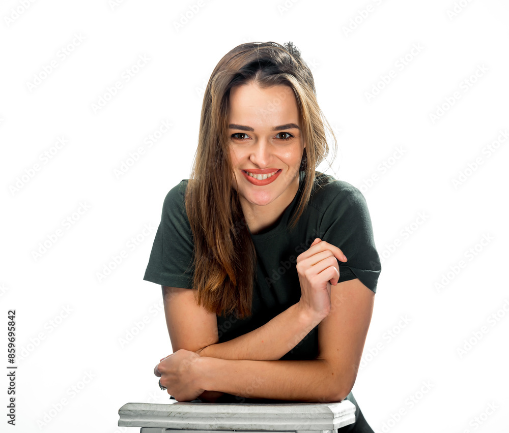Woman Smiling in Studio Portrait. A woman with long brown hair smiles and leans on a white surface in a studio setting. She is wearing a dark green t-shirt. Woman Smiling in Studio Portrait. A woman with long brown hair smiles and leans on a white surface in a studio setting. She is wearing a dark green t-shirt.