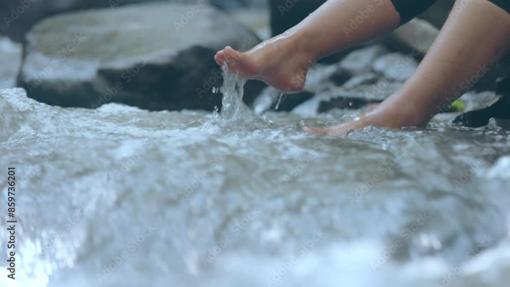 Woman sitting beside waterfall and dangling legs into water and splashing water with fun. Woman sitting beside waterfall and dangling legs into water and splashing water with fun.