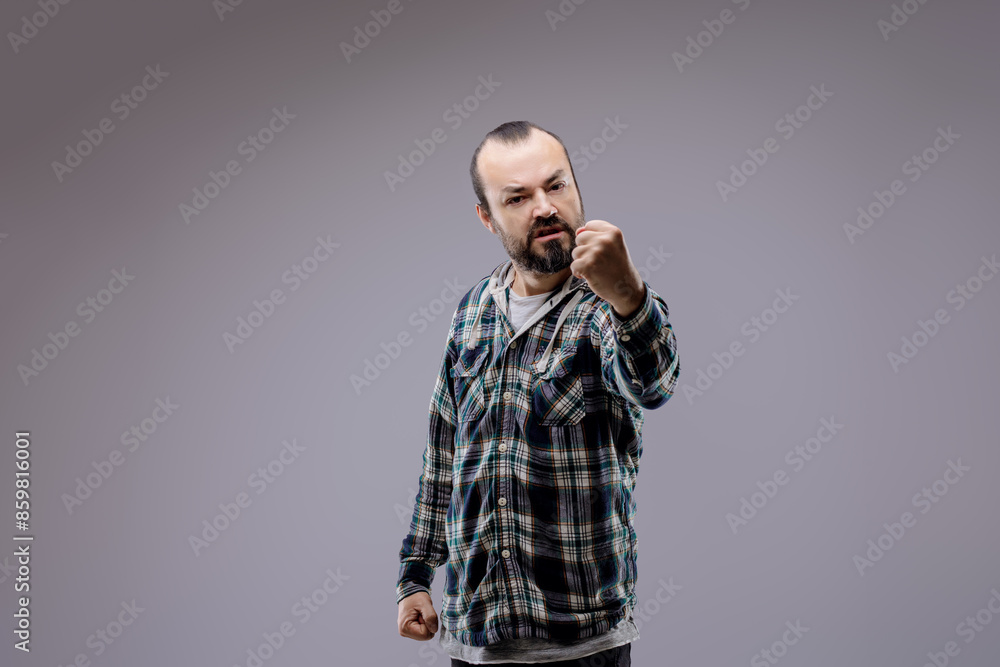Aggressive bearded man raising fists showing anger on grey backg Aggressive bearded man raising fists showing anger on grey backg