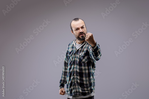 Fotografia Aggressive bearded man raising fists showing anger on grey backg
