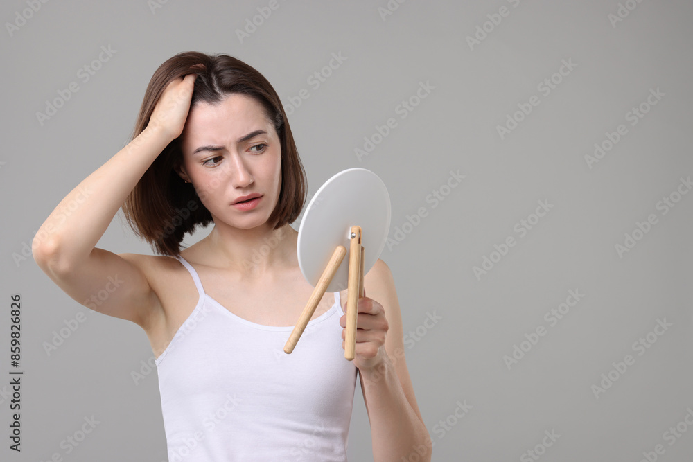 Sad woman with hair loss problem looking at mirror on grey background. Space for text Sad woman with hair loss problem looking at mirror on grey background. Space for text