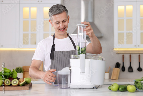 Принти на полотні Smiling man with fresh products using juicer at white marble table in kitchen
