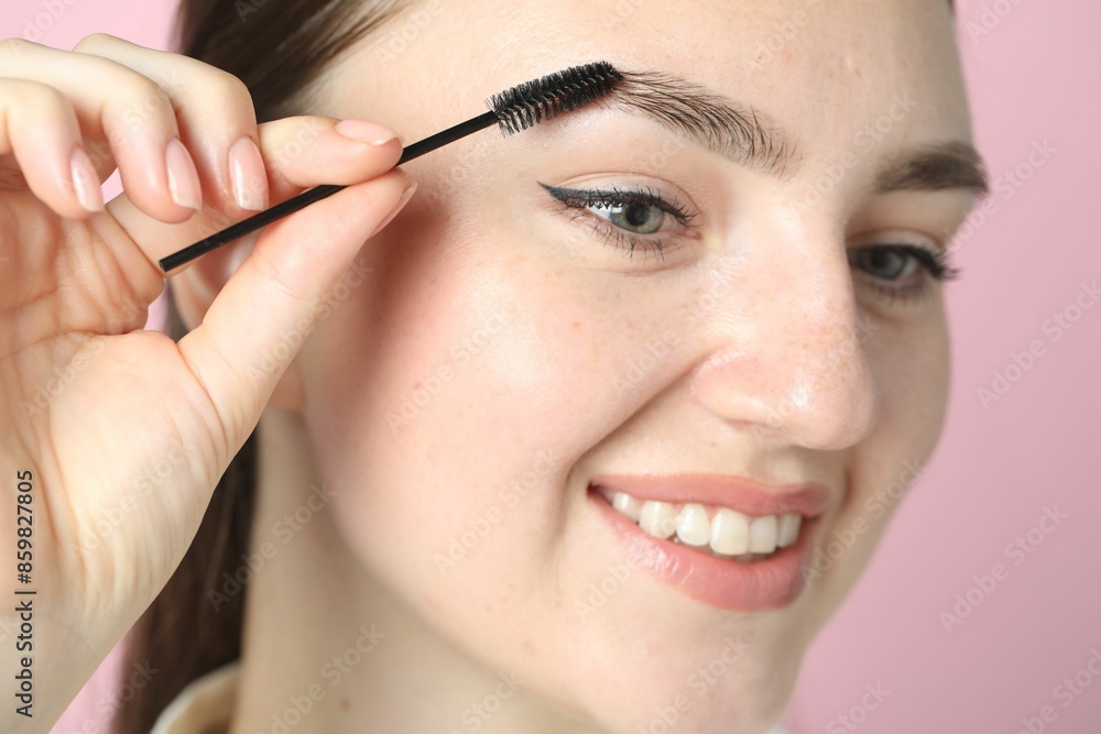 Young woman brushing eyebrow on pink background, closeup Young woman brushing eyebrow on pink background, closeup