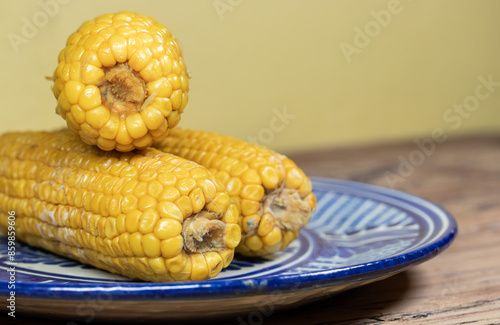 Elote, Maíz amarillo hervido sobre plato de talavera azul en mesa de madera antigua, 