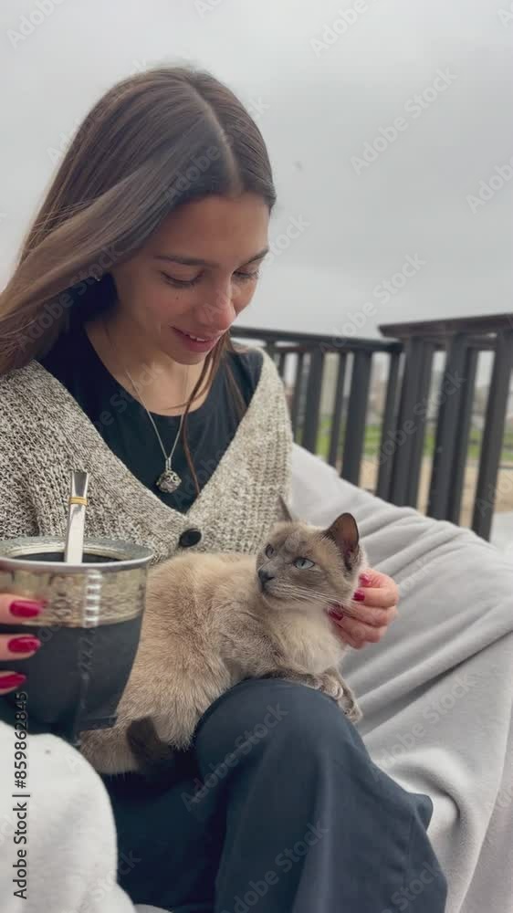 young pretty woman with Yerba Mate petting her cat and sitting on balcony on a cloudy autumn day young pretty woman with Yerba Mate petting her cat and sitting on balcony on a cloudy autumn day