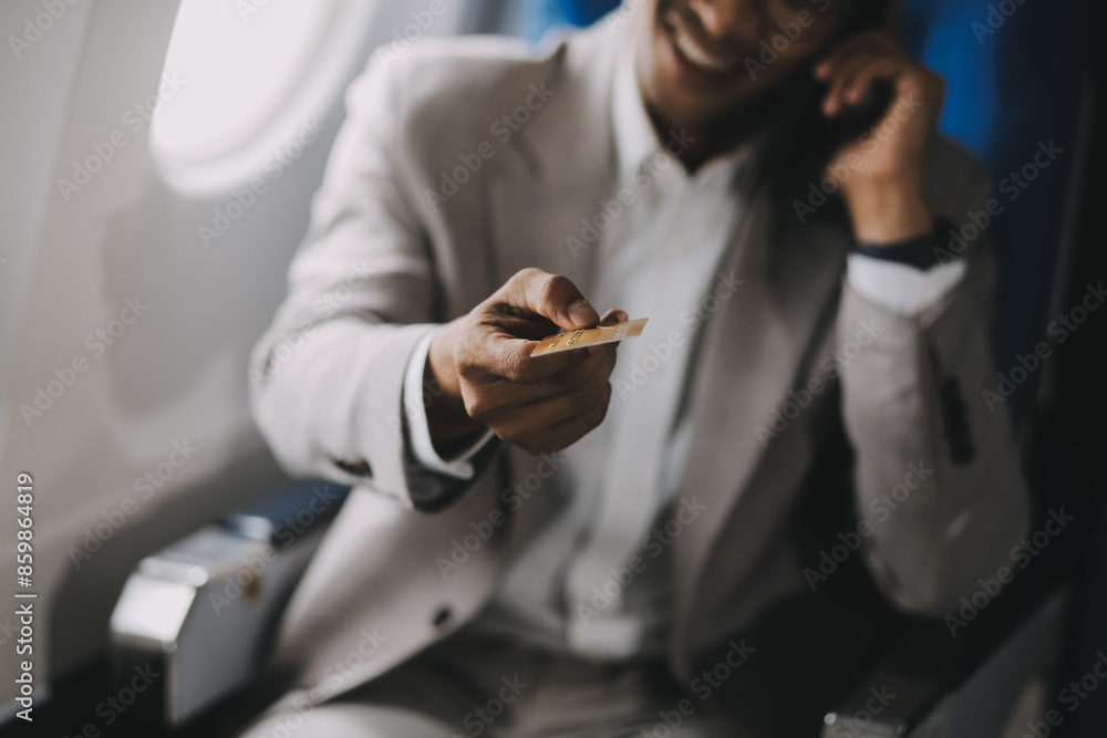 Businessman holding credit card and looking at camera near laptop in private jet Businessman holding credit card and looking at camera near laptop in private jet