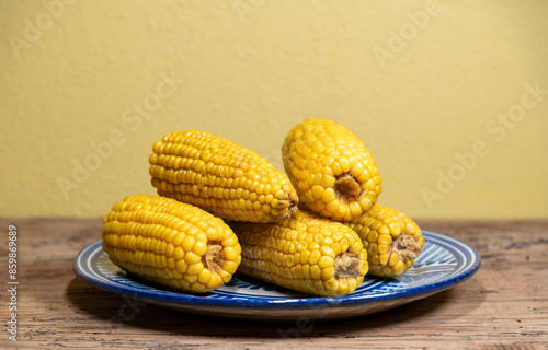 Elote amarillo hervido sobre plato de talavera en mesa de madera vieja color oscuro fondo amarillo 