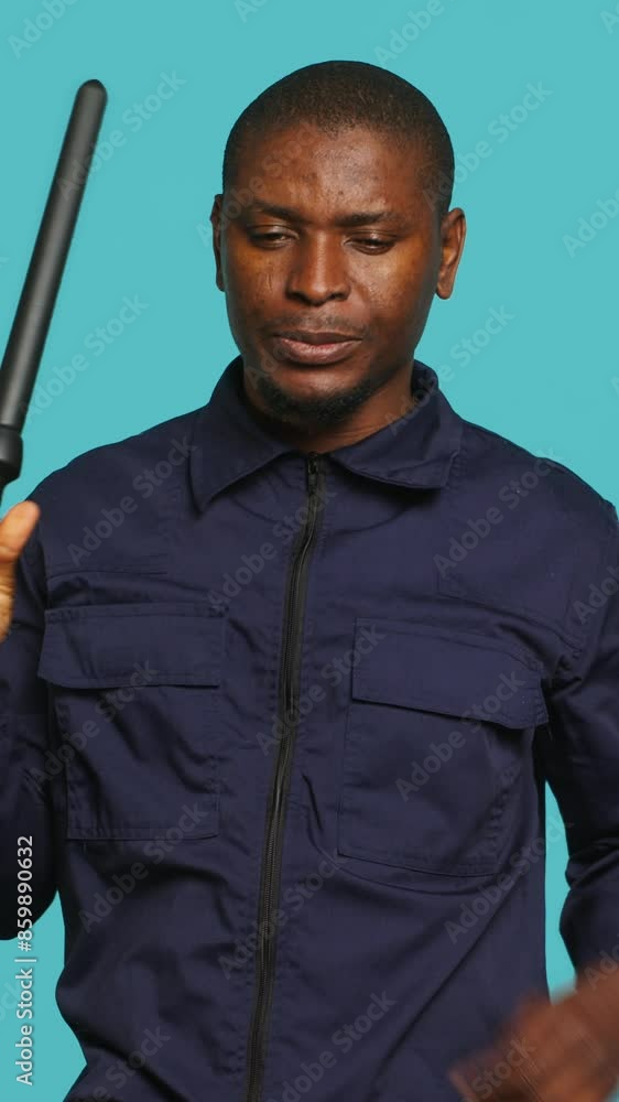 Vertical video Portrait of security guard scratching head with baton while overseeing premises, thinking. Pensive private law enforcement worker daydreaming, rubbing chin, studio backdrop, camera A Vertical video Portrait of security guard scratching head with baton while overseeing premises, thinking. Pensive private law enforcement worker daydreaming, rubbing chin, studio backdrop, camera A