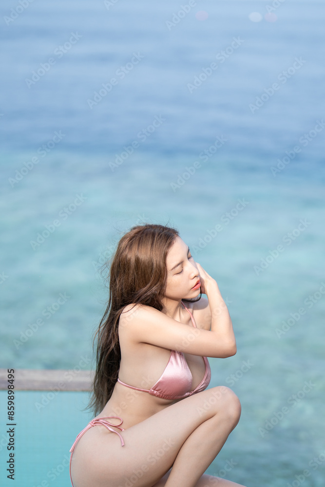 Woman in pink gold swimsuit sitting by the pool on overwater villa in Maldives. Woman in pink gold swimsuit sitting by the pool on overwater villa in Maldives.