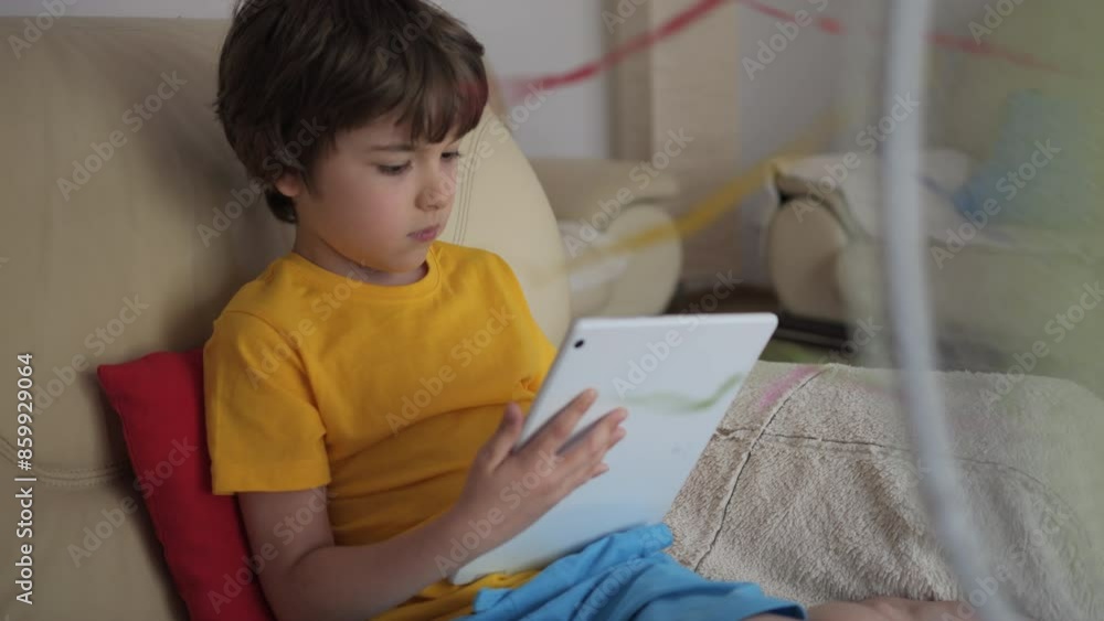 Boy Browsing Social Media on Tablet PC on Hot Heat Summer Day While Sitting on Sofa Near Fan. Child Plays Games on Tablet PC in Heat Weather Near Fan. Cool Wind From Electric Fan at Summer Heat. Boy Browsing Social Media on Tablet PC on Hot Heat Summer Day While Sitting on Sofa Near Fan. Child Plays Games on Tablet PC in Heat Weather Near Fan. Cool Wind From Electric Fan at Summer Heat.
