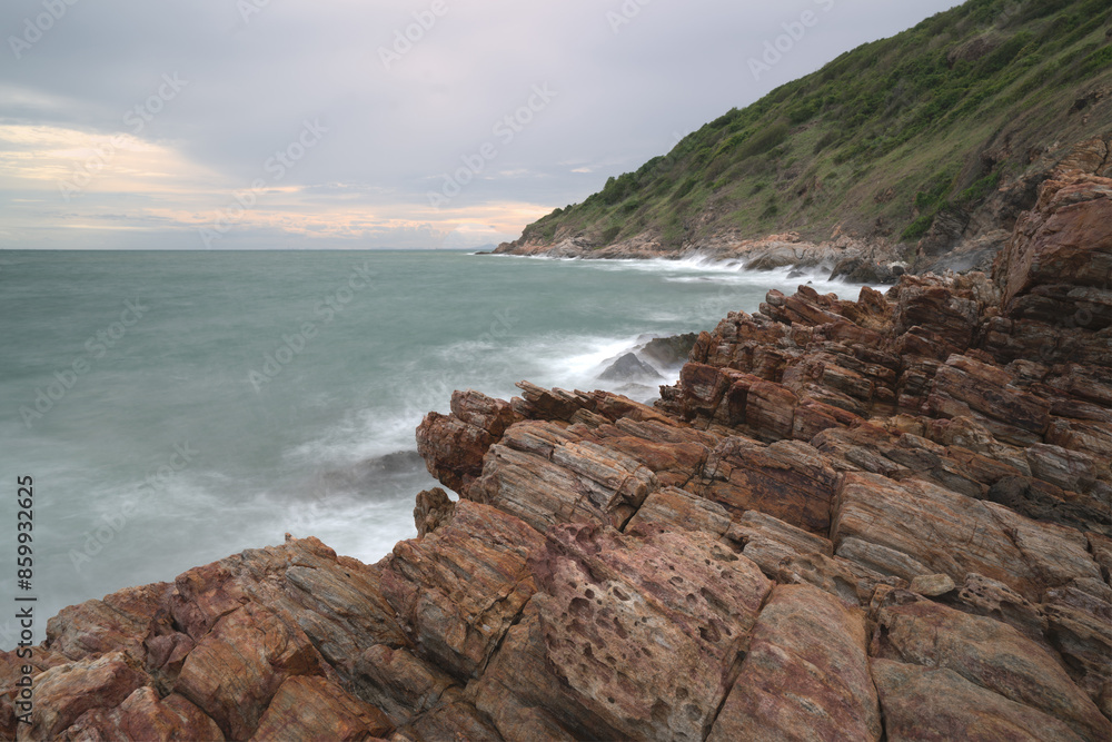 Waves crash against a rocky shoreline with mountains in the background Waves crash against a rocky shoreline with mountains in the background