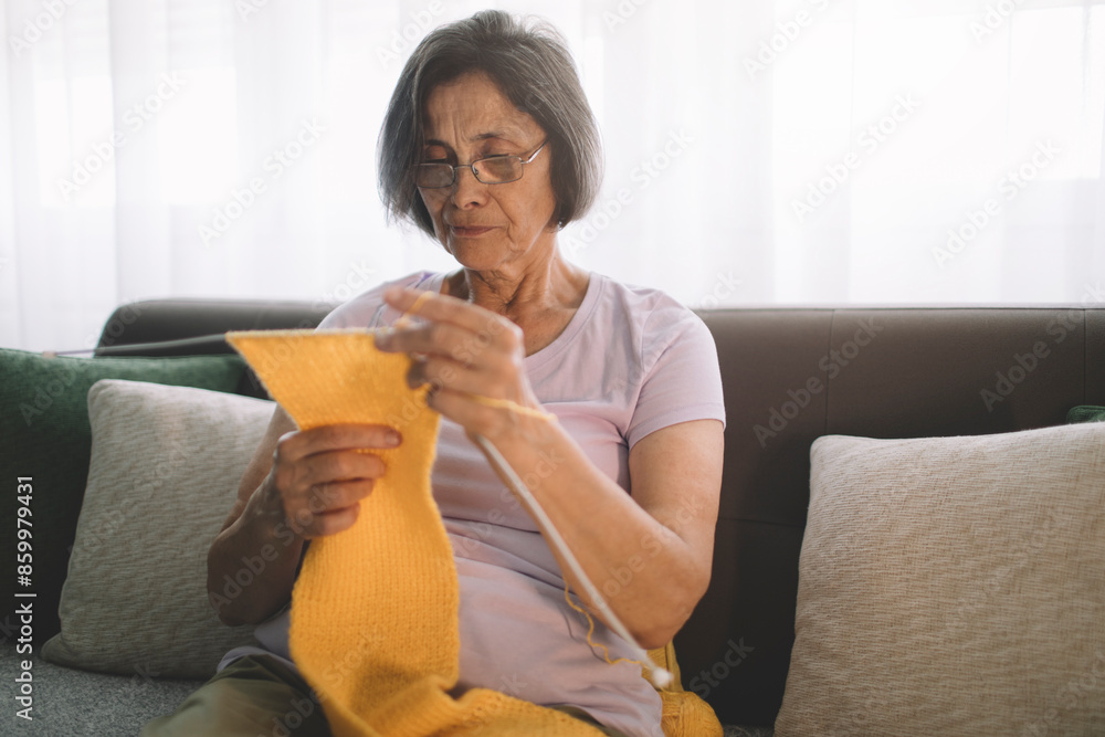 Portrait of mature woman in casual clothes, wearing eyeglasses knitting warm yellow scarf for her grandchild Portrait of mature woman in casual clothes, wearing eyeglasses knitting warm yellow scarf for her grandchild