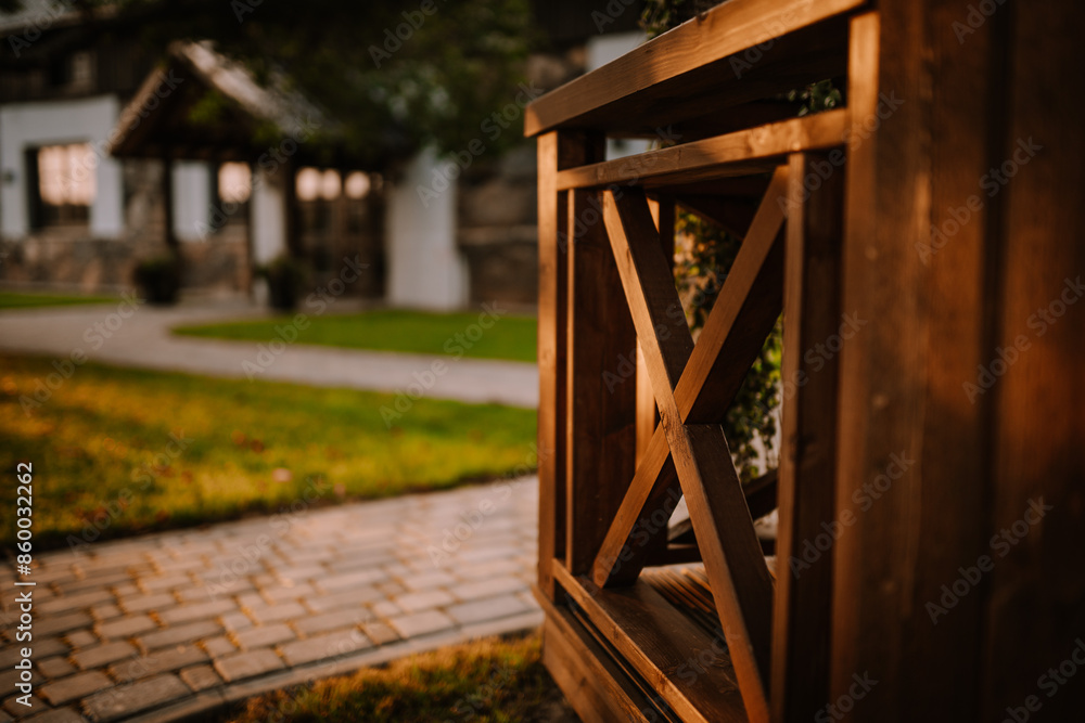 Blome, Latvia - September 11, 2023 - Close-up of a wooden fence with an X design, with a blurred view of a stone house and green lawn in the background. Copy space... Blome, Latvia - September 11, 2023 - Close-up of a wooden fence with an X design, with a blurred view of a stone house and green lawn in the background. Copy space...